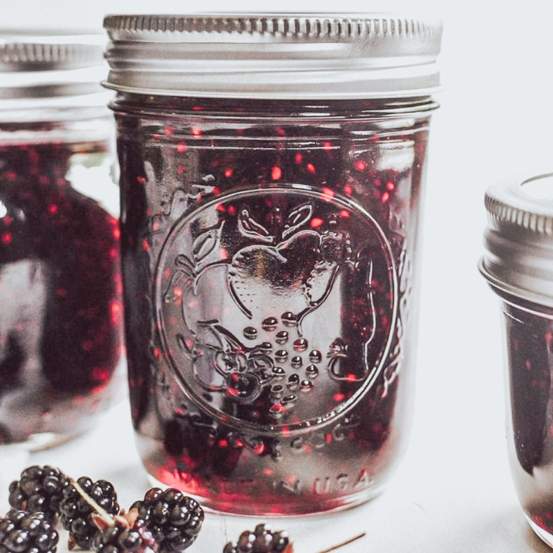 Homemade elderberry jam in a glass mason jar with fresh elderberries on a white background.